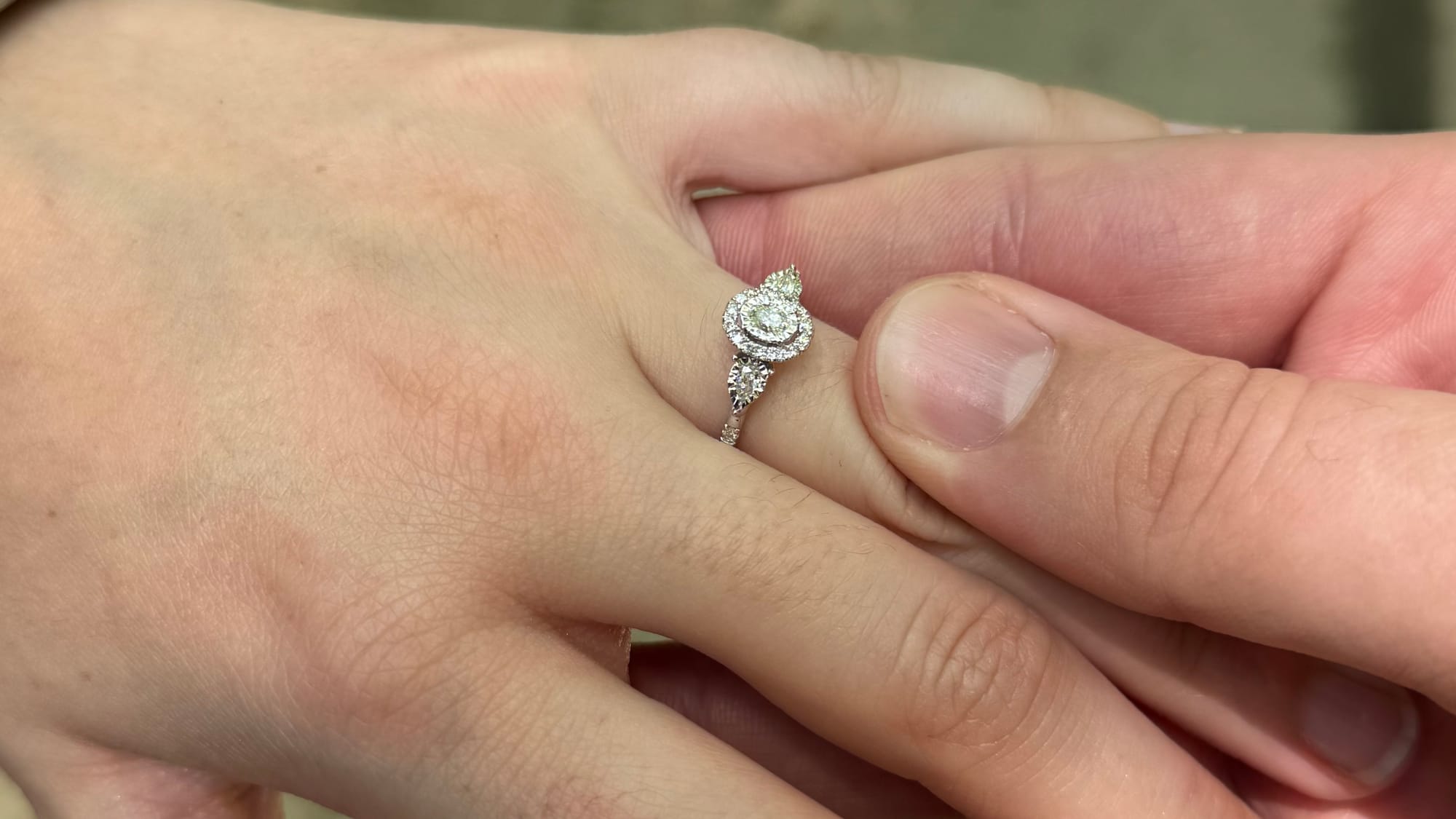 A hand with an engagement ring held by another hand