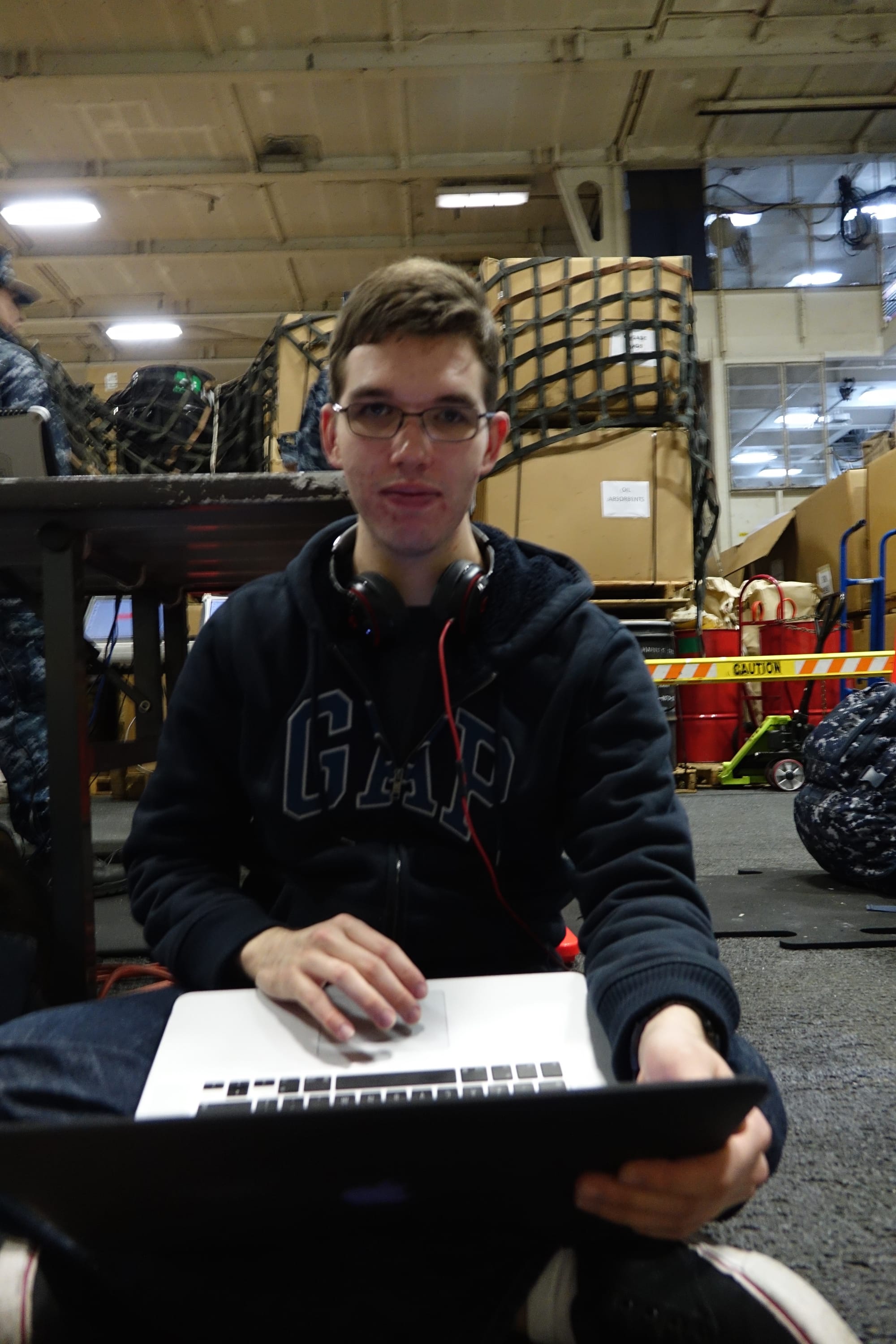 2014 Wesley in an aircraft carrier hanger bay on a MacBook Pro wearing wired Beats headphones