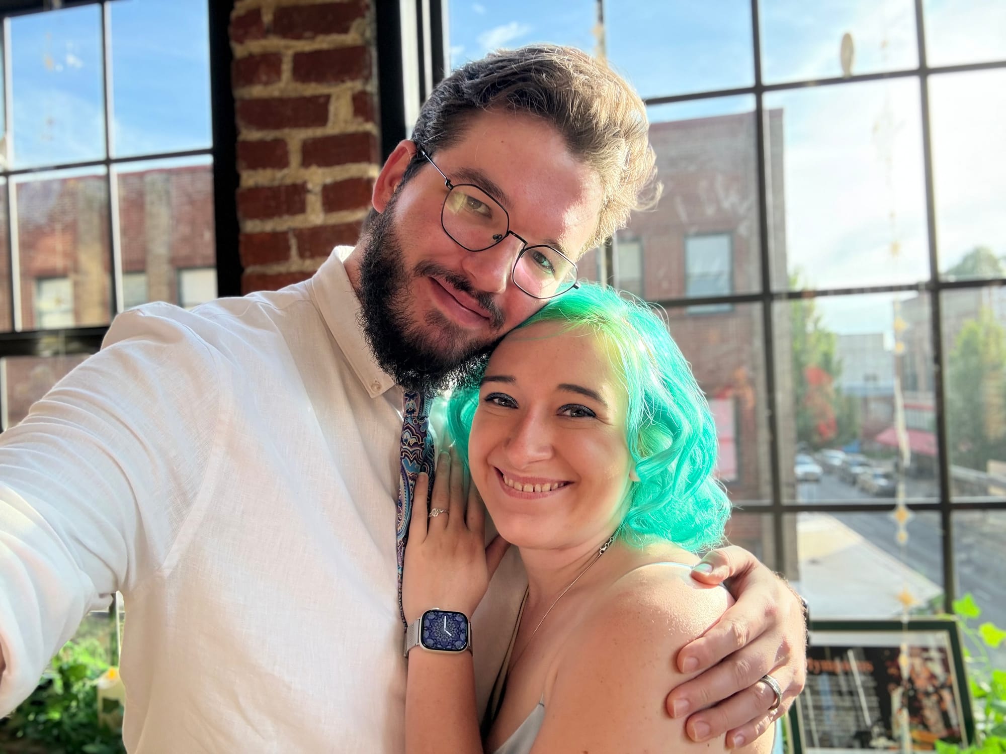 A photo of Wesley wearing a button up white shirt and tie holding Natalie with her green hair and strappy dress