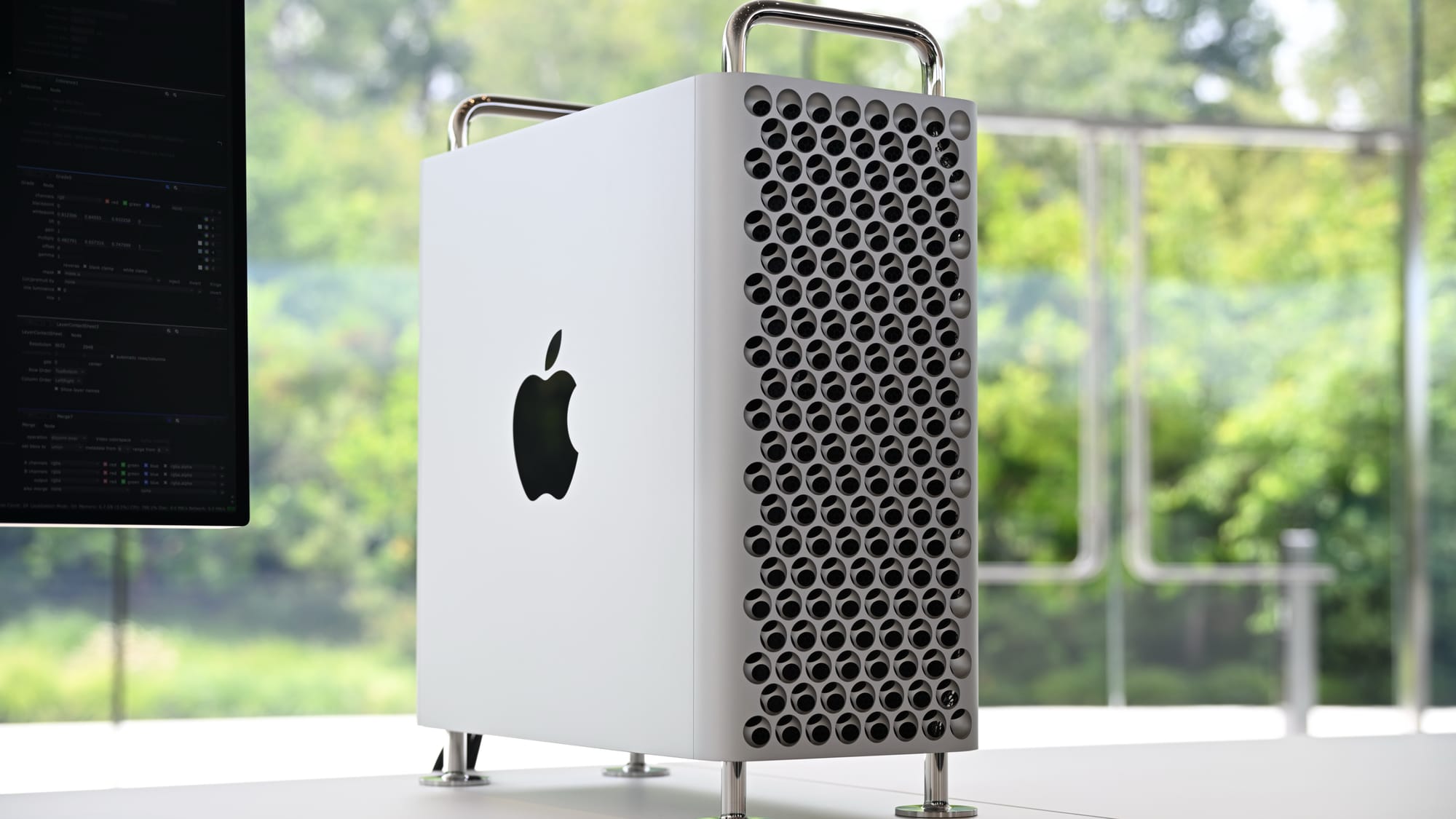 A Mac Pro on a table with a window in the background showing green trees and grass